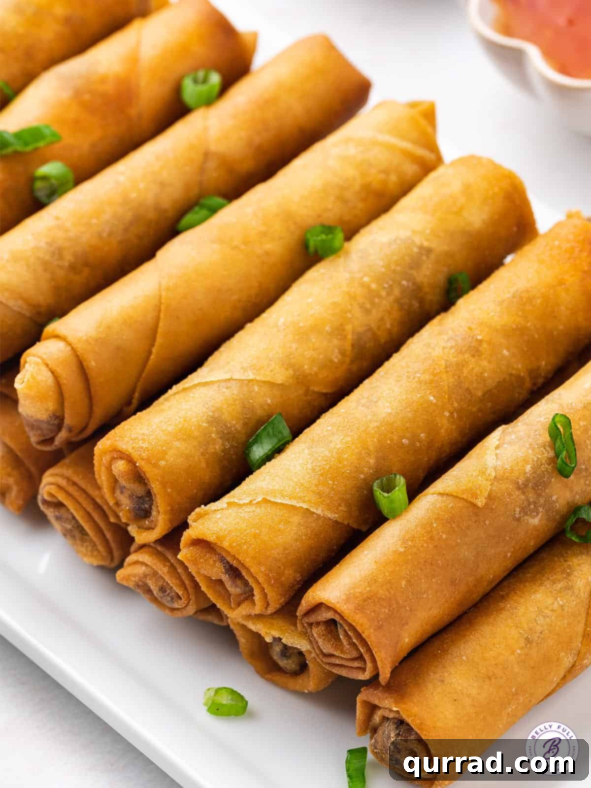 This lumpia recipe features a ground pork and water chestnut filling in a thin wrapper that's fried to perfection. Homemade lumpia arranged neatly on a white serving tray.