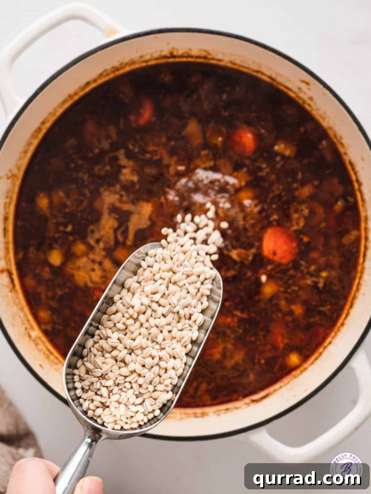 Close-up of pearl barley being poured into a pot of beef and barley soup.