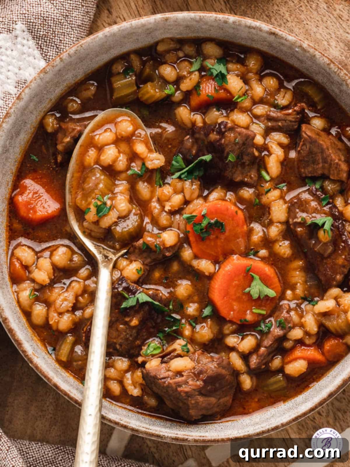 A close-up of a spoon lifting a spoonful of beef barley soup, showcasing tender meat and barley.