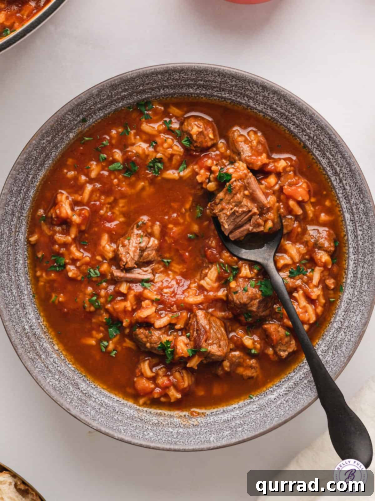 Overhead view of a comforting bowl of tomato soup with rice and a spoon.