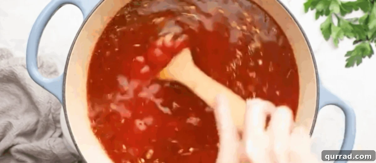 Adding all remaining soup ingredients, including crushed tomatoes and beef broth, to the pot.