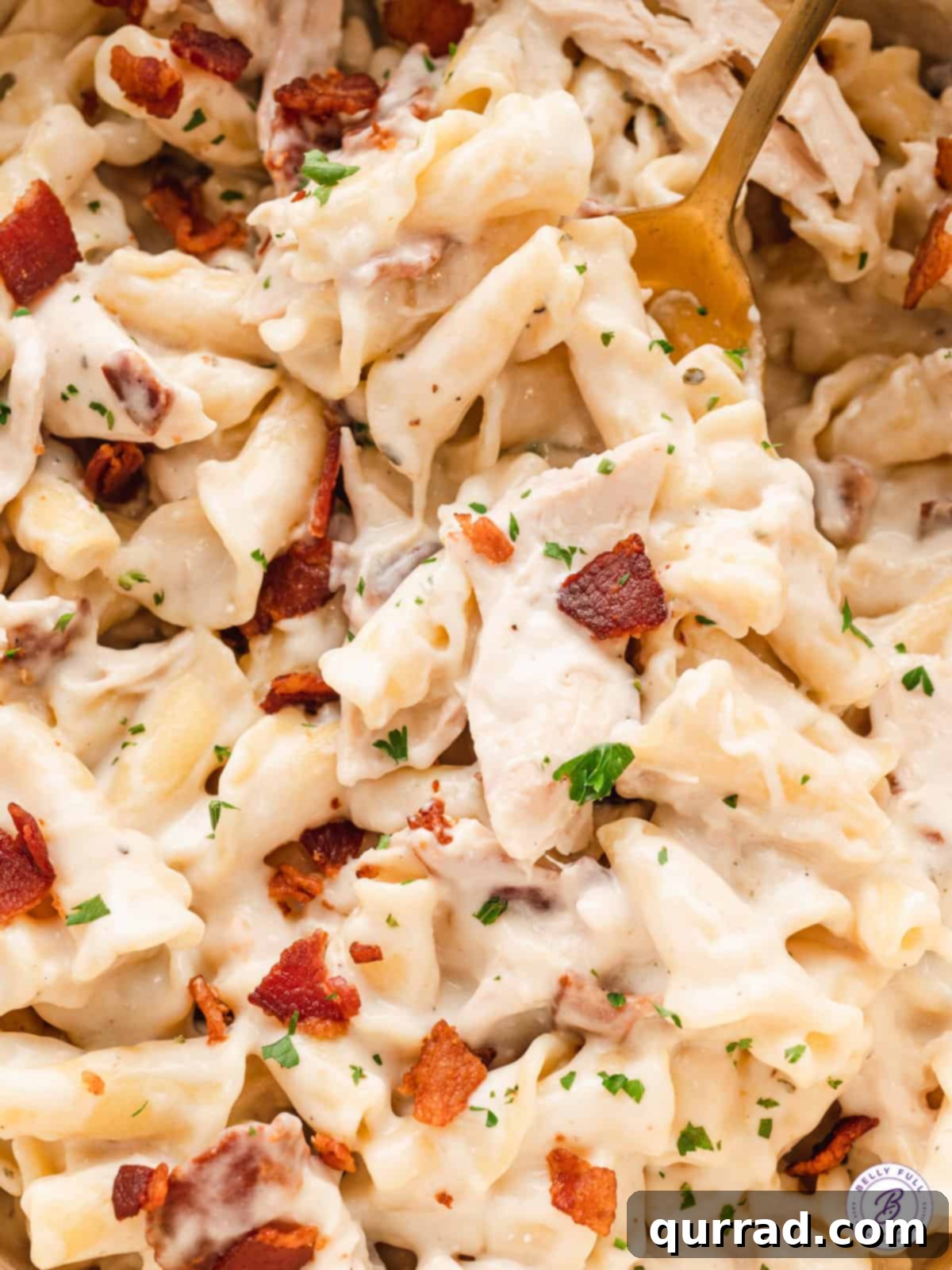 This Chicken Bacon Ranch Pasta is creamy and cheesy with pieces of shredded rotisserie chicken and salty thick-cut bacon. A gold fork lifting chicken bacon ranch pasta out of a bowl.