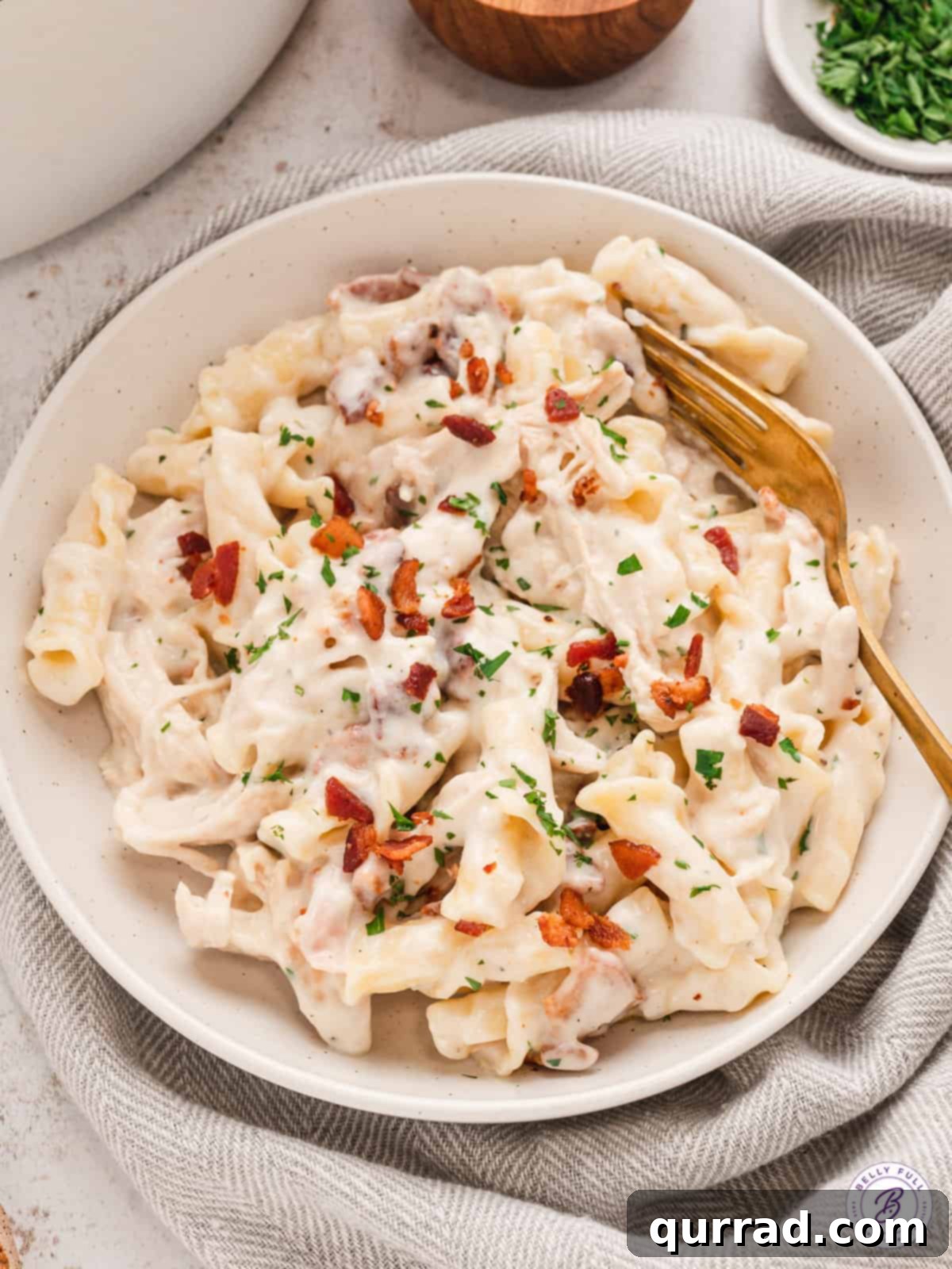 This Chicken Bacon Ranch Pasta is creamy and cheesy with pieces of shredded rotisserie chicken and salty thick-cut bacon. A bowl of chicken bacon ranch pasta on a white plate with a gold fork.