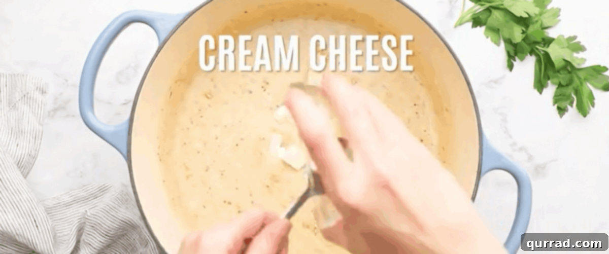 Loaded Chicken Bacon Ranch Pasta 6 Adding cheeses and seasoning to the roux in a pot with blue handles.