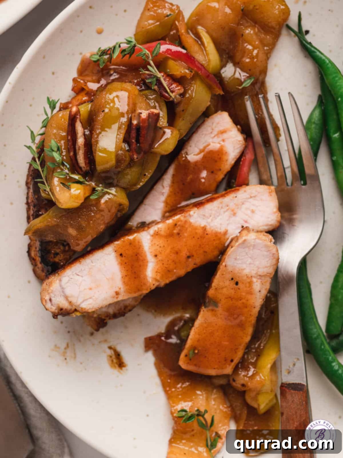A plate of gourmet boneless pork chops with apples, artfully sliced and ready to savor. A beautifully presented sliced pork chop with caramelized apples on a pristine white plate, garnished with fresh thyme.