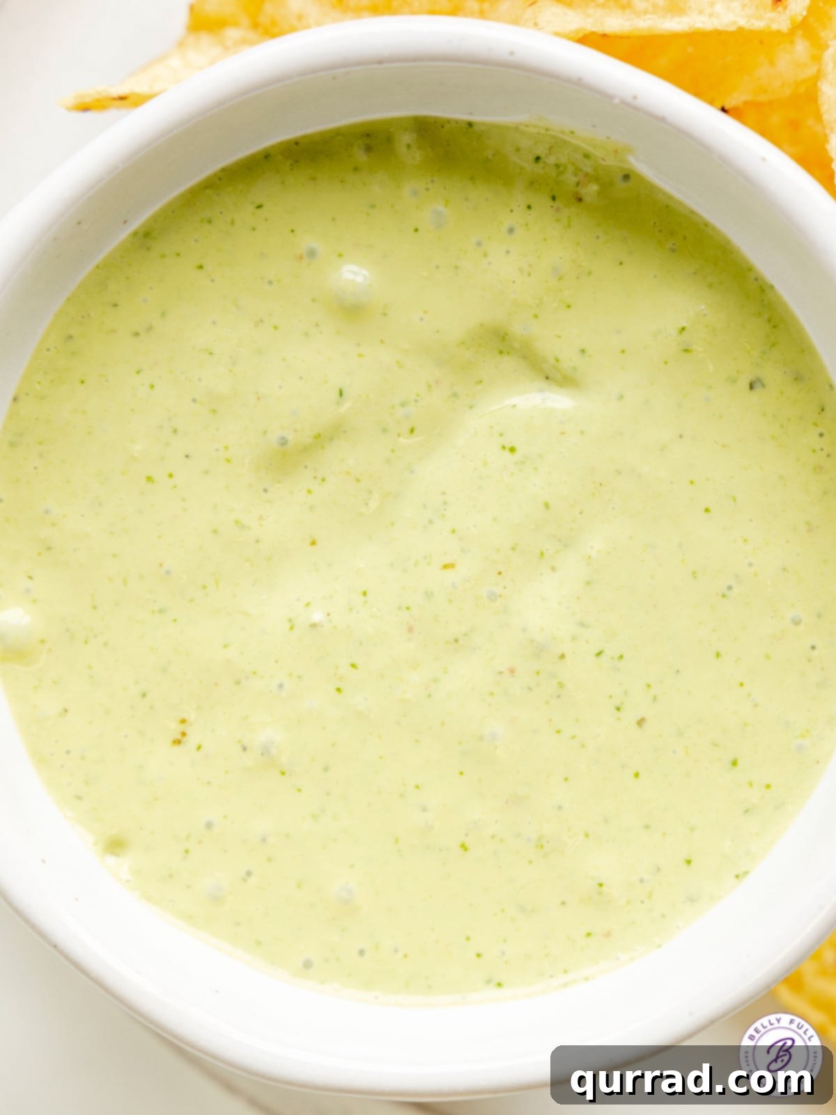 A close-up shot of the rich, smooth, and inviting creamy blended jalapeño dip in a white ceramic bowl, highlighting its perfect texture and fresh green flecks.