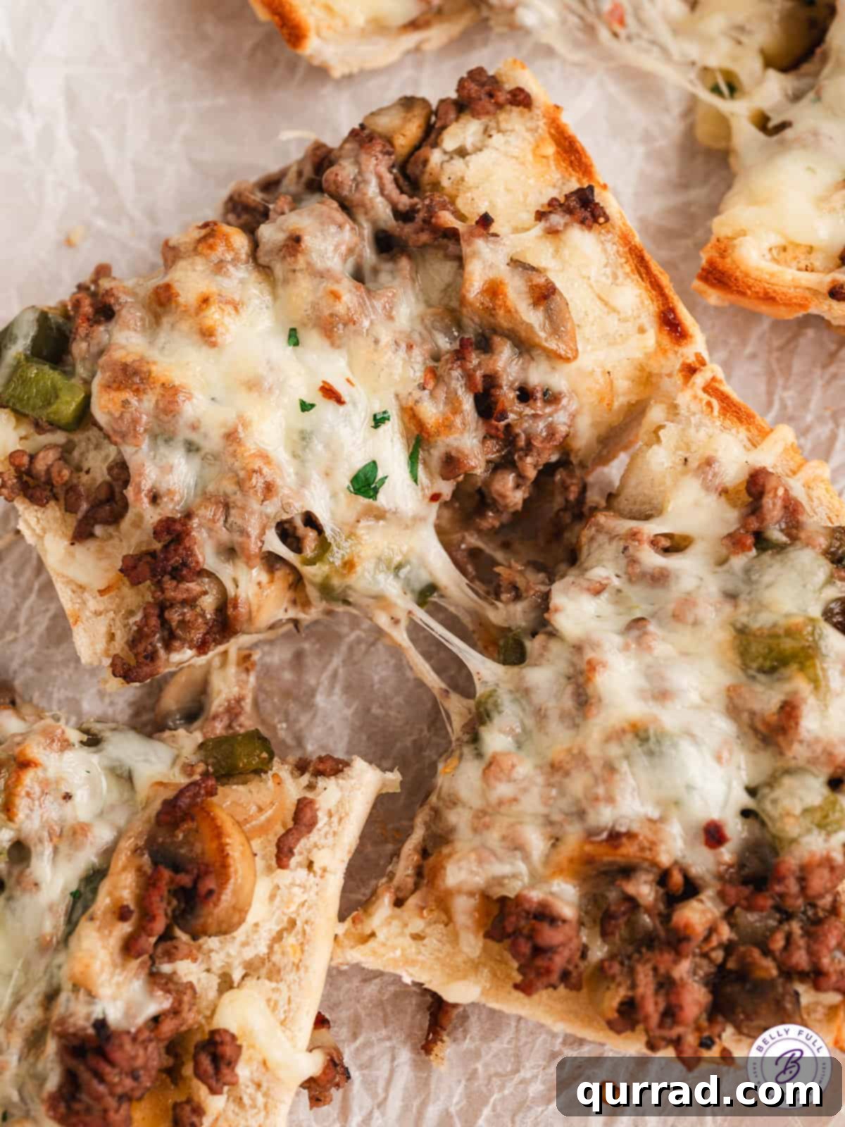 Two slices of Philly cheesesteak bread being pulled apart, revealing gooey cheese and savory filling
