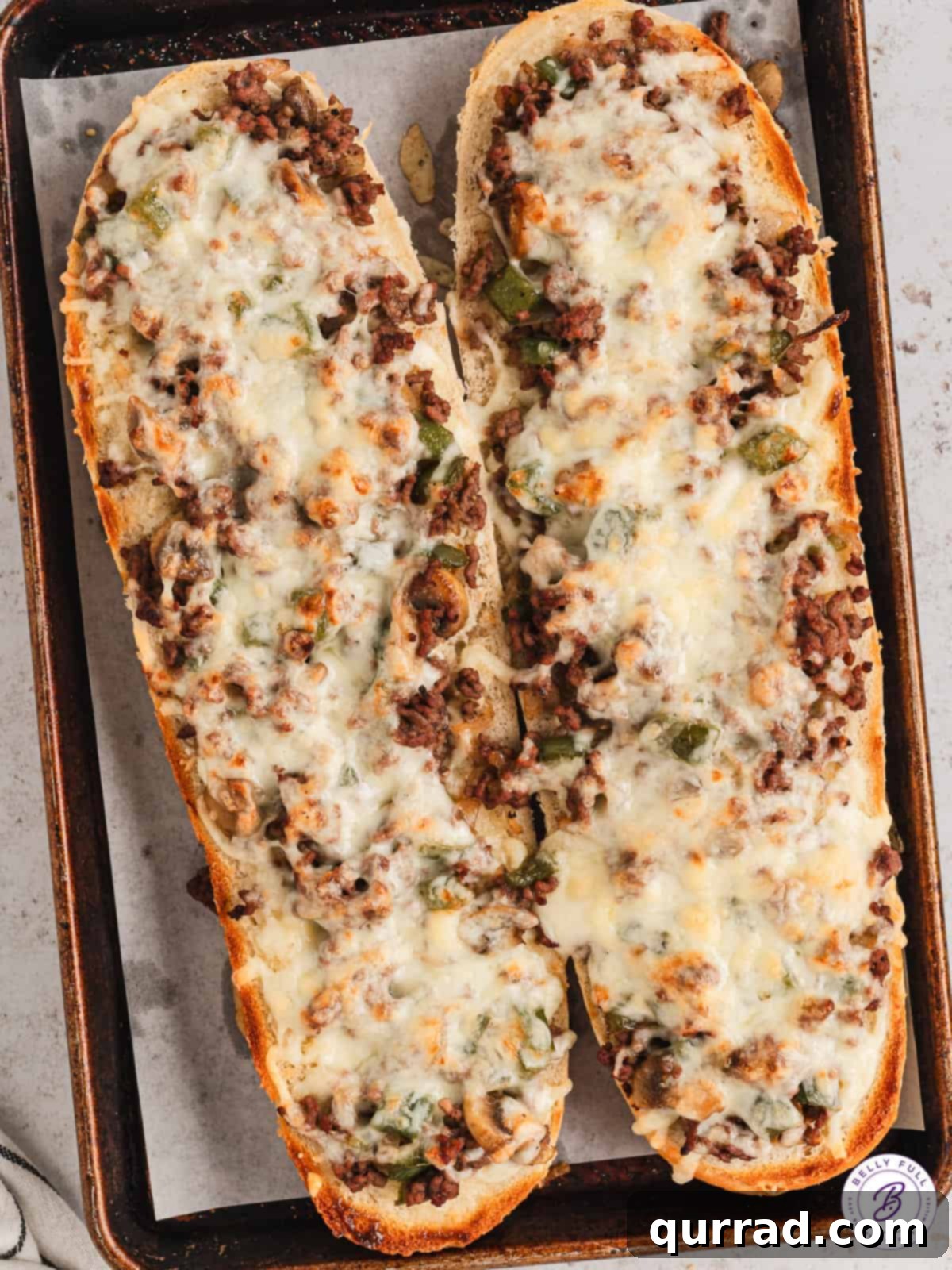 Overhead view of two golden-brown loaves of Philly cheesesteak cheesy bread, fresh from the oven