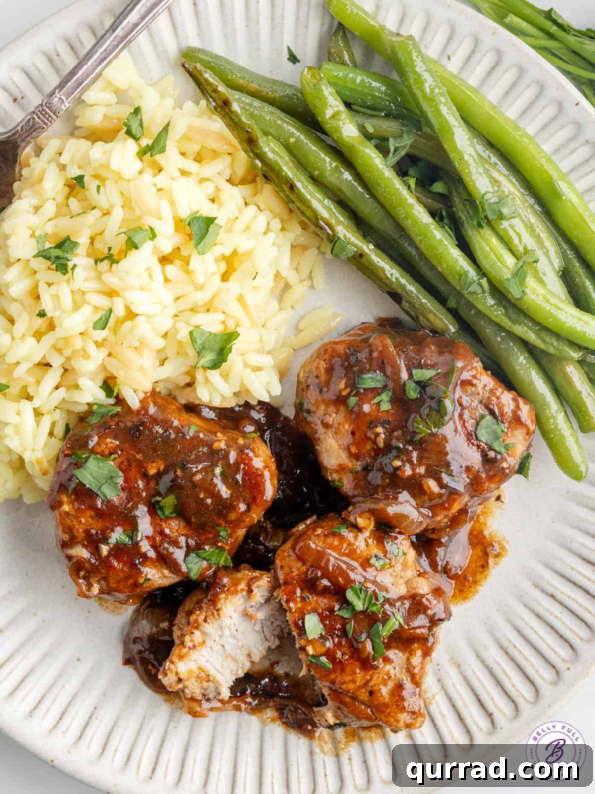 Pork Medallions Dinner Plate Pork medallions served on a white plate with fluffy white rice and vibrant green beans, all drizzled with brown gravy.