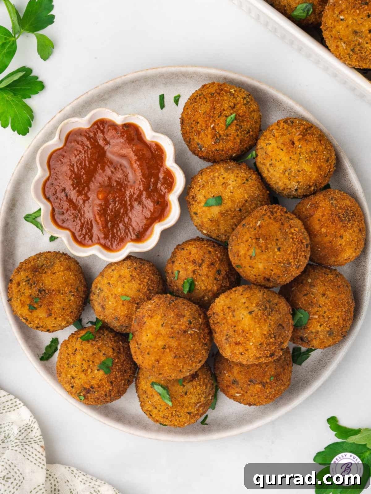 Best Fried Italian Rice Balls with Marinara Sauce An inviting overhead view of a platter of freshly fried Arancini, sprinkled with fresh parsley and served with a side dish of rich marinara sauce.