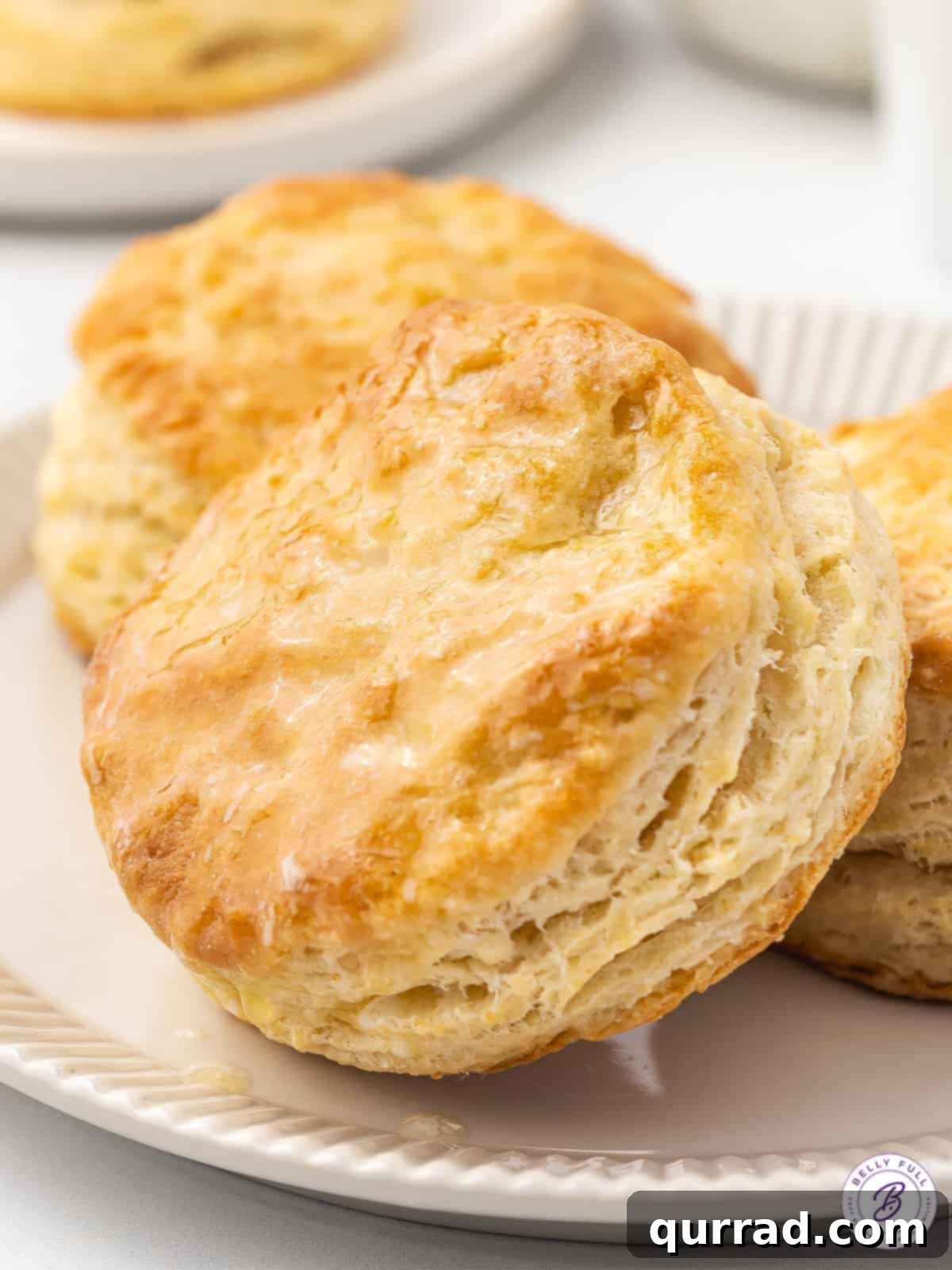 Soft, flaky, and buttery, these Easy Homemade Biscuits are made with just 6 ingredients in 30 minutes. The perfect biscuit recipe! Close up of perfectly golden homemade buttermilk biscuits on a white plate, showcasing their soft, flaky layers.
