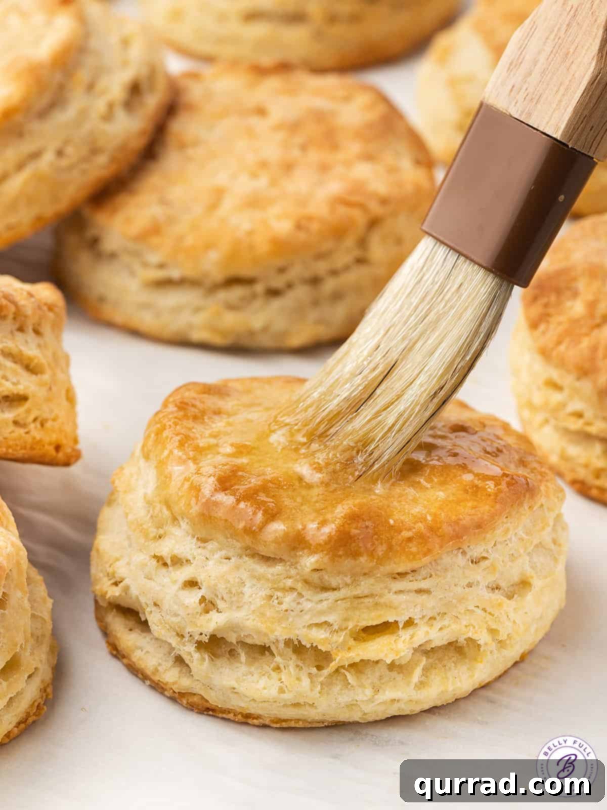 Soft, flaky, and buttery, these Easy Homemade Biscuits are made with just 6 ingredients in 30 minutes. The perfect biscuit recipe! Freshly baked homemade biscuits with melted butter being brushed over their golden-brown tops, enhancing their richness and sheen.