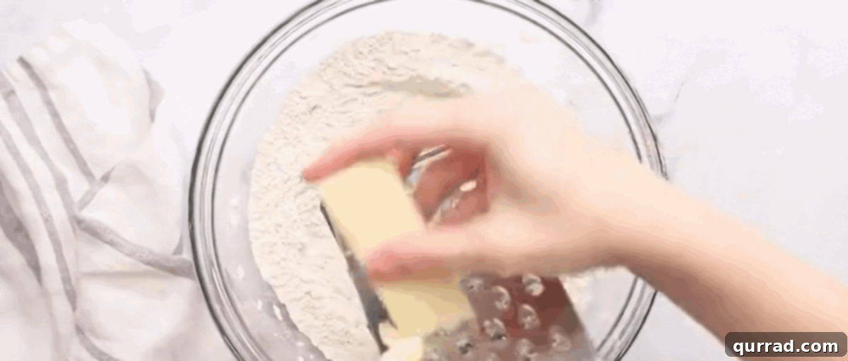 Buttery Flaky Homemade Biscuits 4 Grating the frozen unsalted butter directly into the bowl of dry ingredients, preparing to cut it in for flaky biscuits.