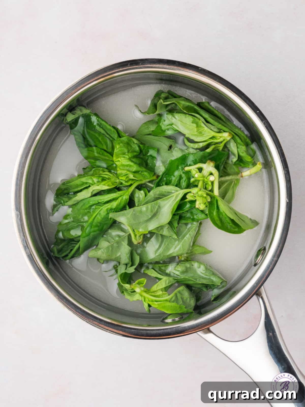 This Basil Simple Syrup is a great way to add sweet, earthy flavor to any cocktail or drink. Made with just 3 ingredients! Basil leaves in simple syrup in a saucepan
