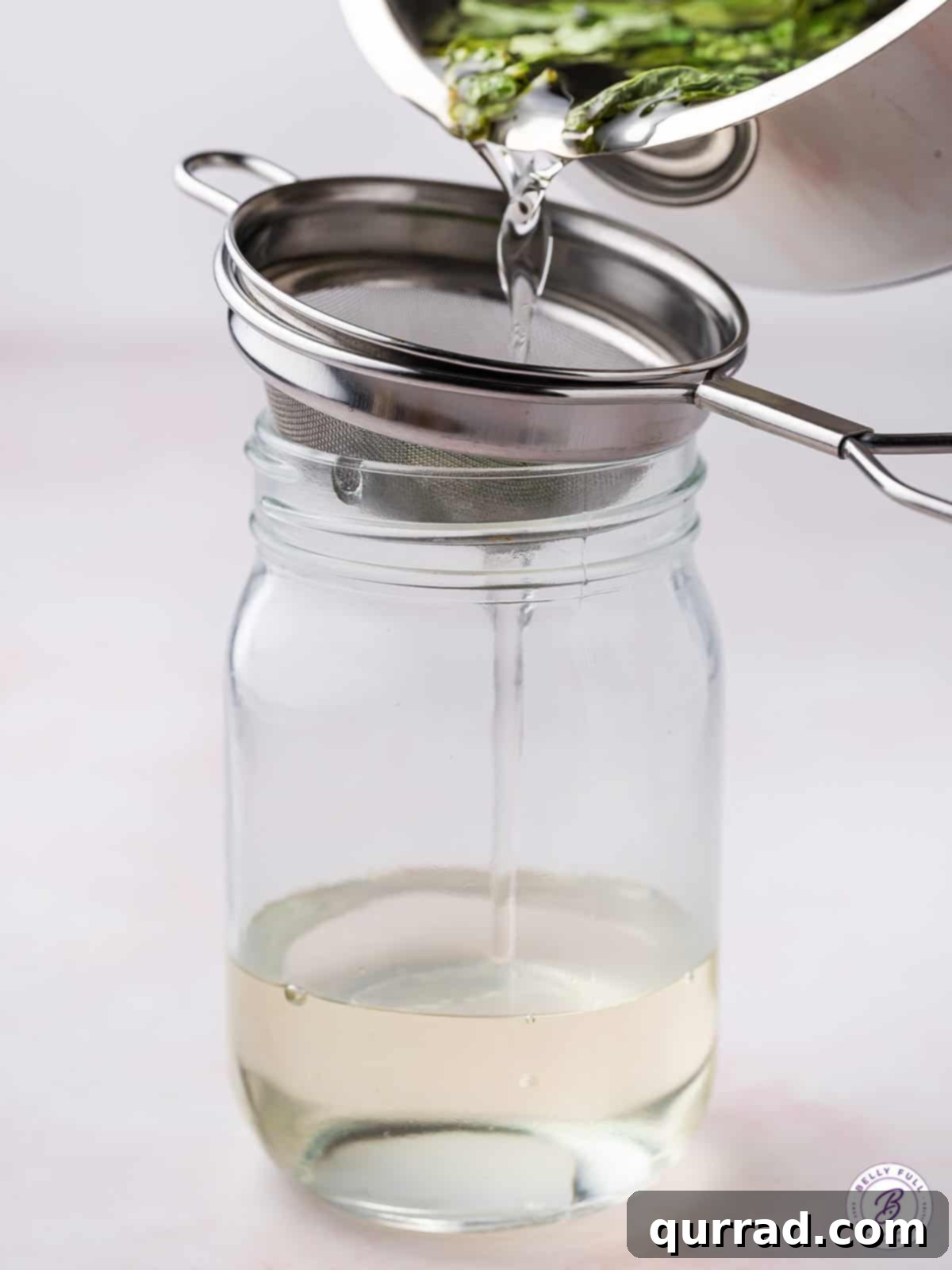 This Basil Simple Syrup is a great way to add sweet, earthy flavor to any cocktail or drink. Made with just 3 ingredients! Basil simple syrup being strained into a glass jar