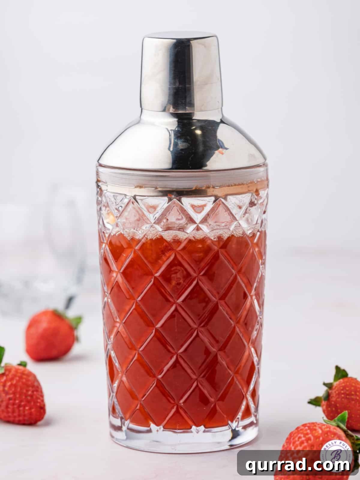 All the key ingredients for the Ski Ya Later Cocktail expertly combined in a shaker. A cocktail shaker filled with ice and the ingredients for a Ski Ya Later Cocktail, showing the vibrant red liquid.