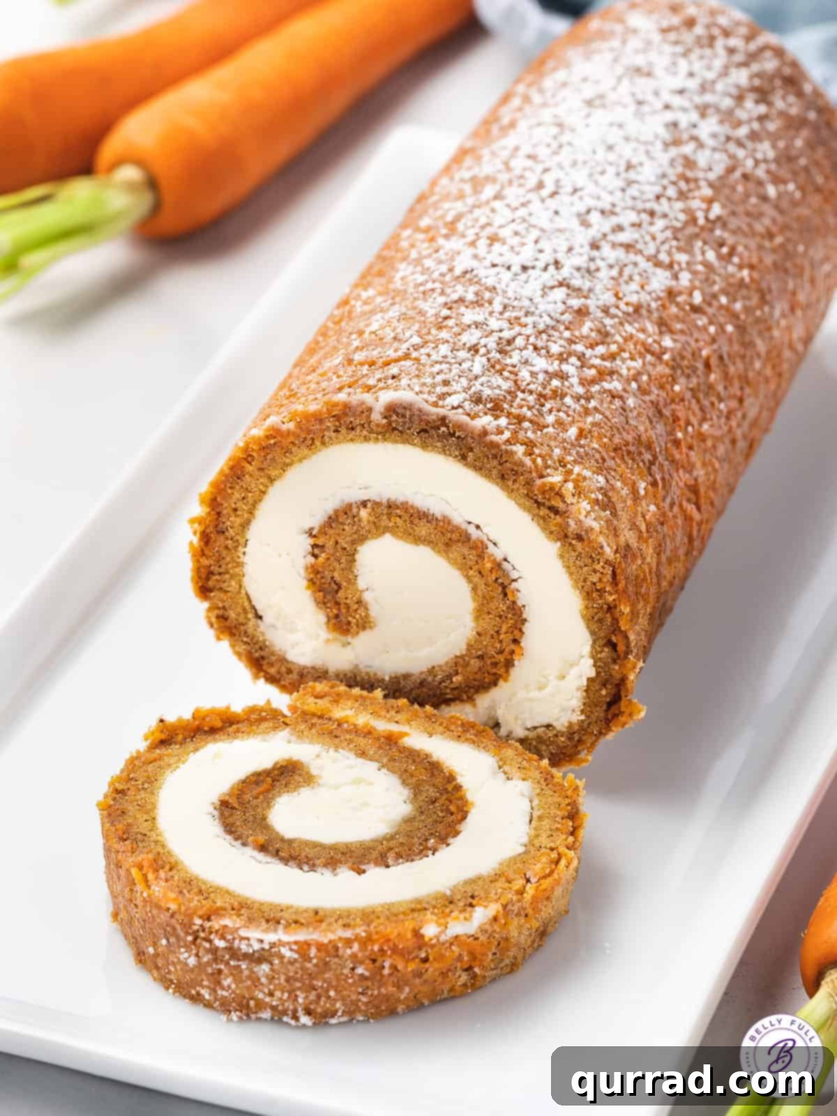 Spiced Carrot Cake Roulade 2 A perfectly sliced carrot cake roll showcasing its creamy filling on a pristine white plate, garnished with a light dusting of powdered sugar.