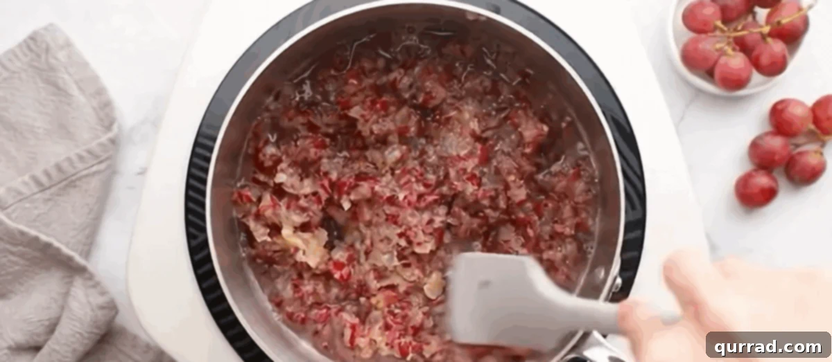 Step 4: Simmering the Filling The coarsely crushed red grapes are simmering gently in a large pot on the stovetop, thickening into a rich filling.
