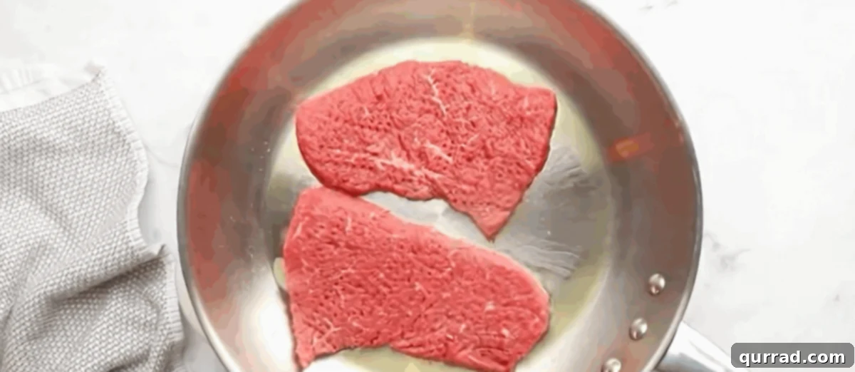 Tender Slow Cooker Cube Steak 3 Searing the steak in a stainless steel pan.