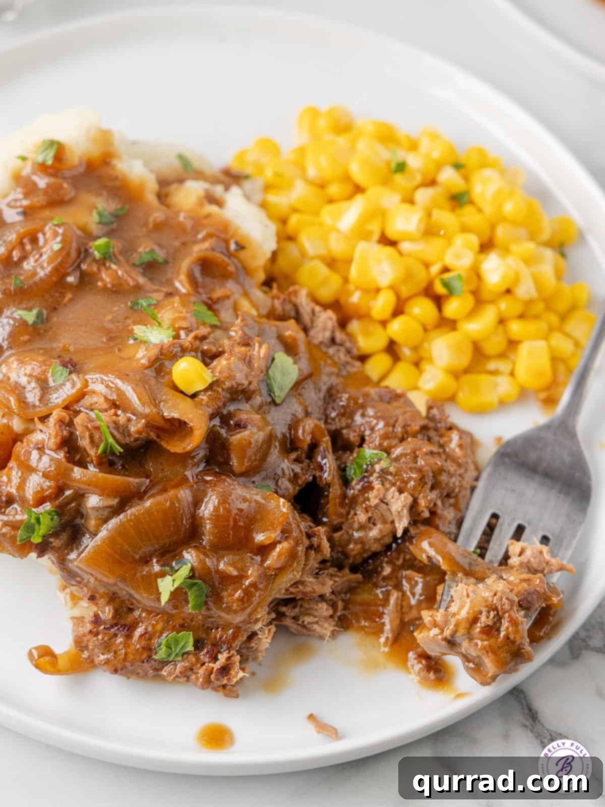 This Slow Cooker Cube Steak recipe features beef cube steaks browned then slow cooked all day with onions, gravy, and cream of mushroom soup. A plate with slow cooker cube steak, mashed potatoes, and corn.