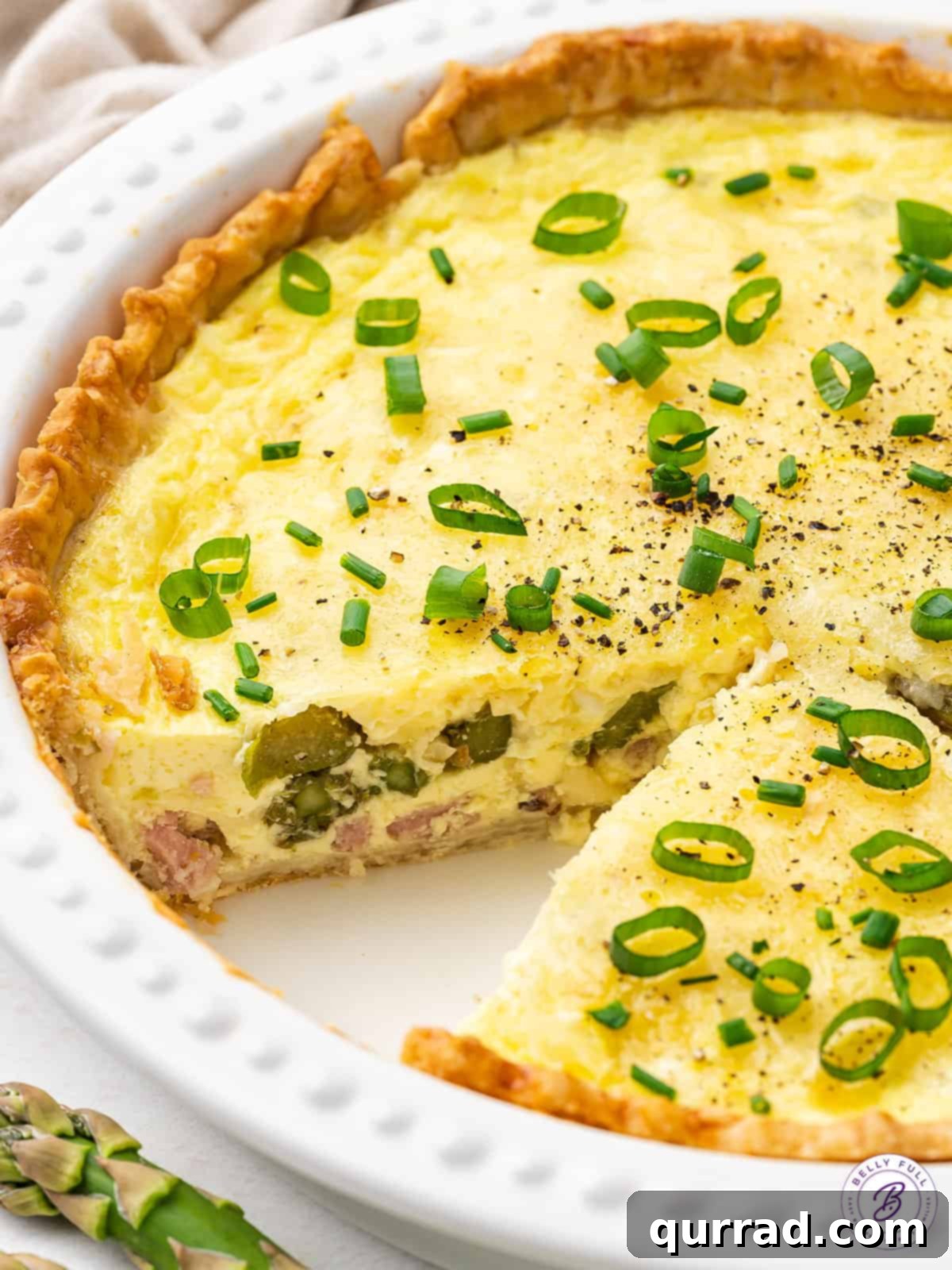 A freshly baked asparagus quiche with one slice already removed, showing the rich layers of filling.