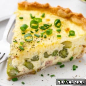 A fresh slice of asparagus quiche on a pristine white plate, showcasing the vibrant green asparagus and golden crust.
