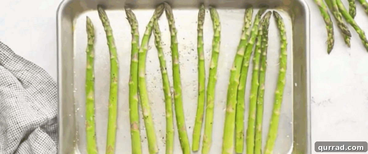 Fresh asparagus spears arranged on a baking sheet, ready for roasting.