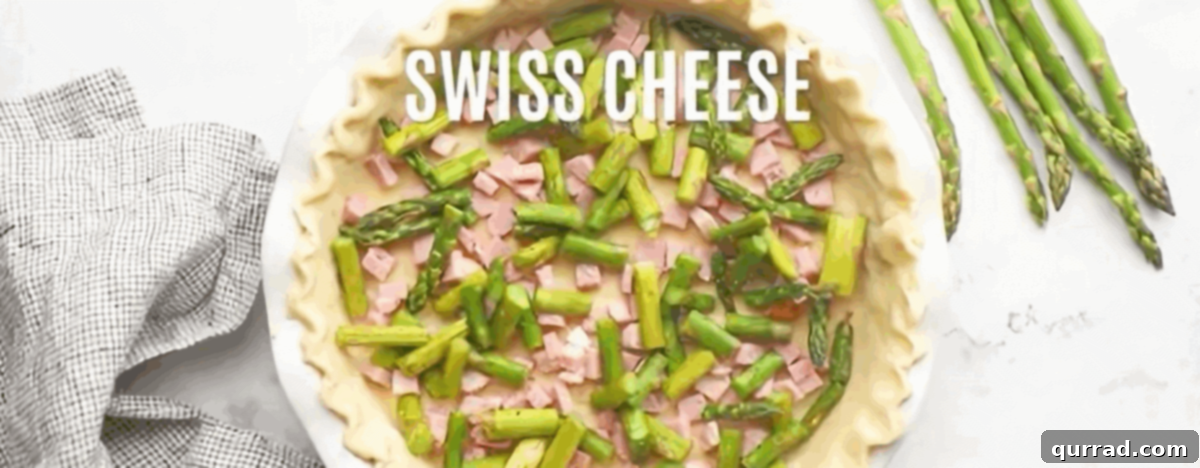 The pie crust filled with layers of diced ham, roasted asparagus, and shredded cheeses, ready for the egg custard.