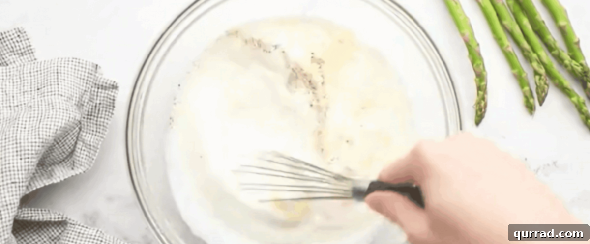 A glass bowl containing whisked eggs, half-and-half, and seasonings, forming the creamy quiche custard.