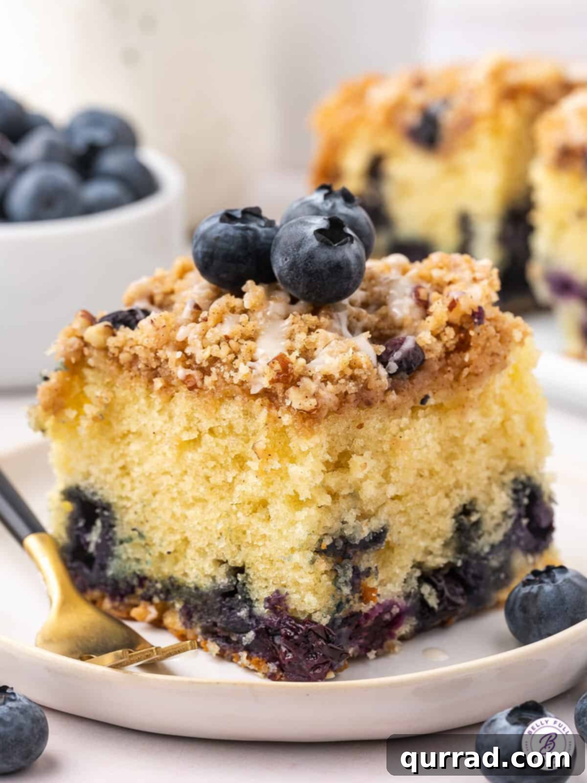 A perfectly sliced piece of blueberry sour cream coffee cake on a white plate, showcasing its moist texture and vibrant blueberries.
