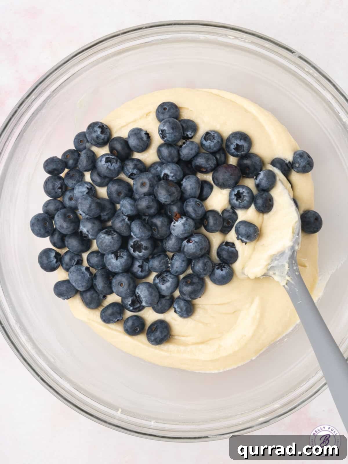 Fresh blueberries gently folded into a rich, creamy coffee cake batter in a mixing bowl, ready for baking.