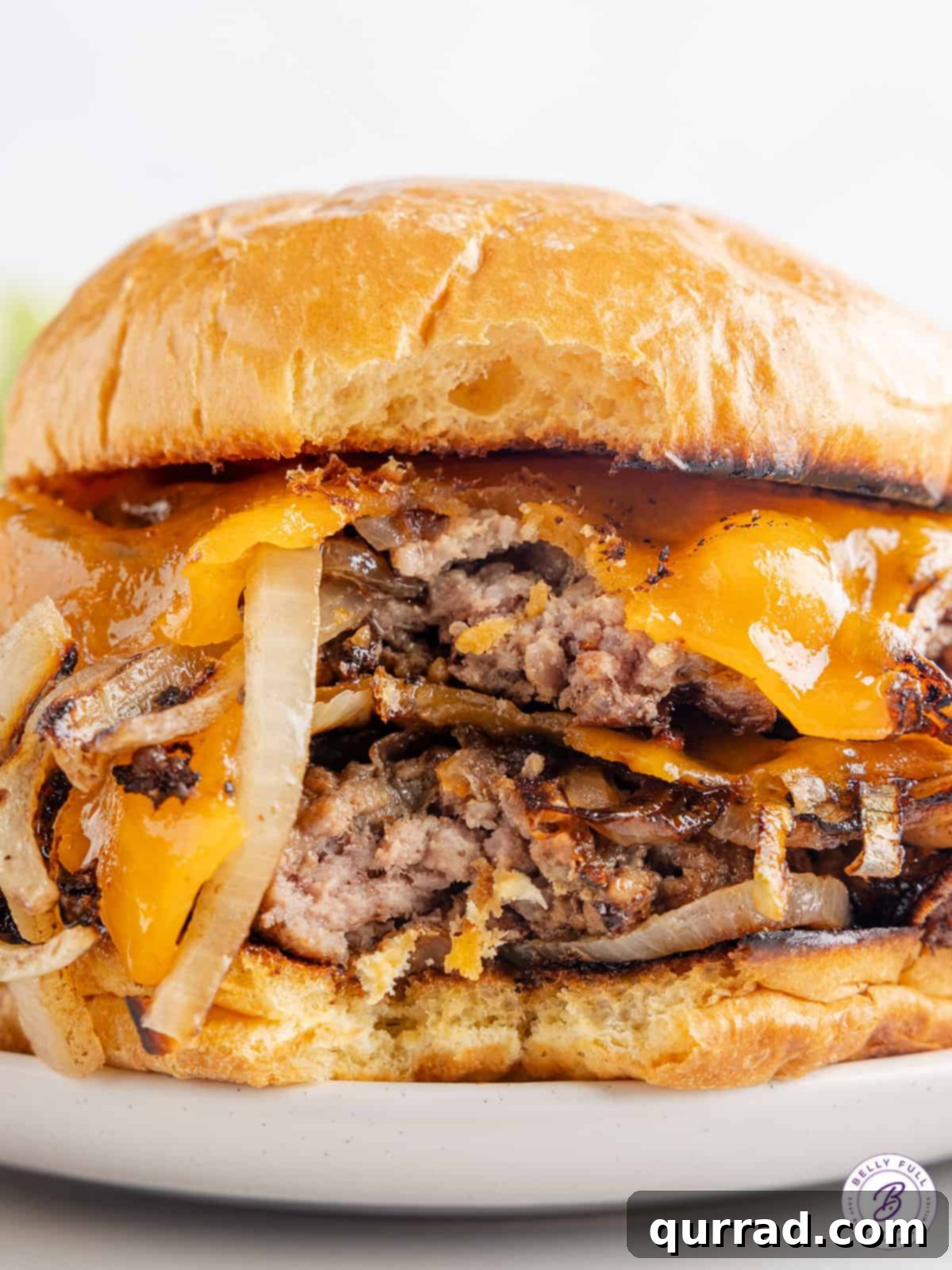 These Oklahoma Smash Burgers are burger patties smashed over thinly sliced onions, until the edges are crisp and the center remains juicy. Close up of a double Oklahoma onion smash burger with two patties on a toasted bun, showing melted cheese and crispy onion-infused edges.