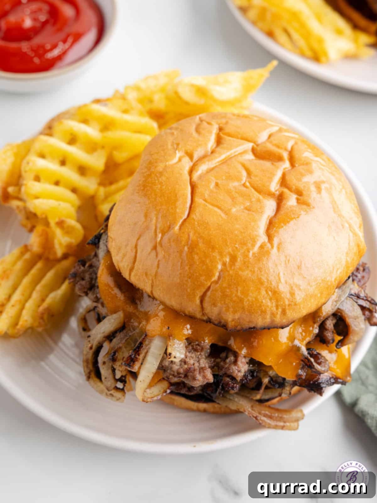 These Oklahoma Smash Burgers are burger patties smashed over thinly sliced onions, until the edges are crisp and the center remains juicy. A perfectly cooked Oklahoma smash burger with two patties, melted cheese, and caramelized onions, served on a plate with crispy waffle fries.