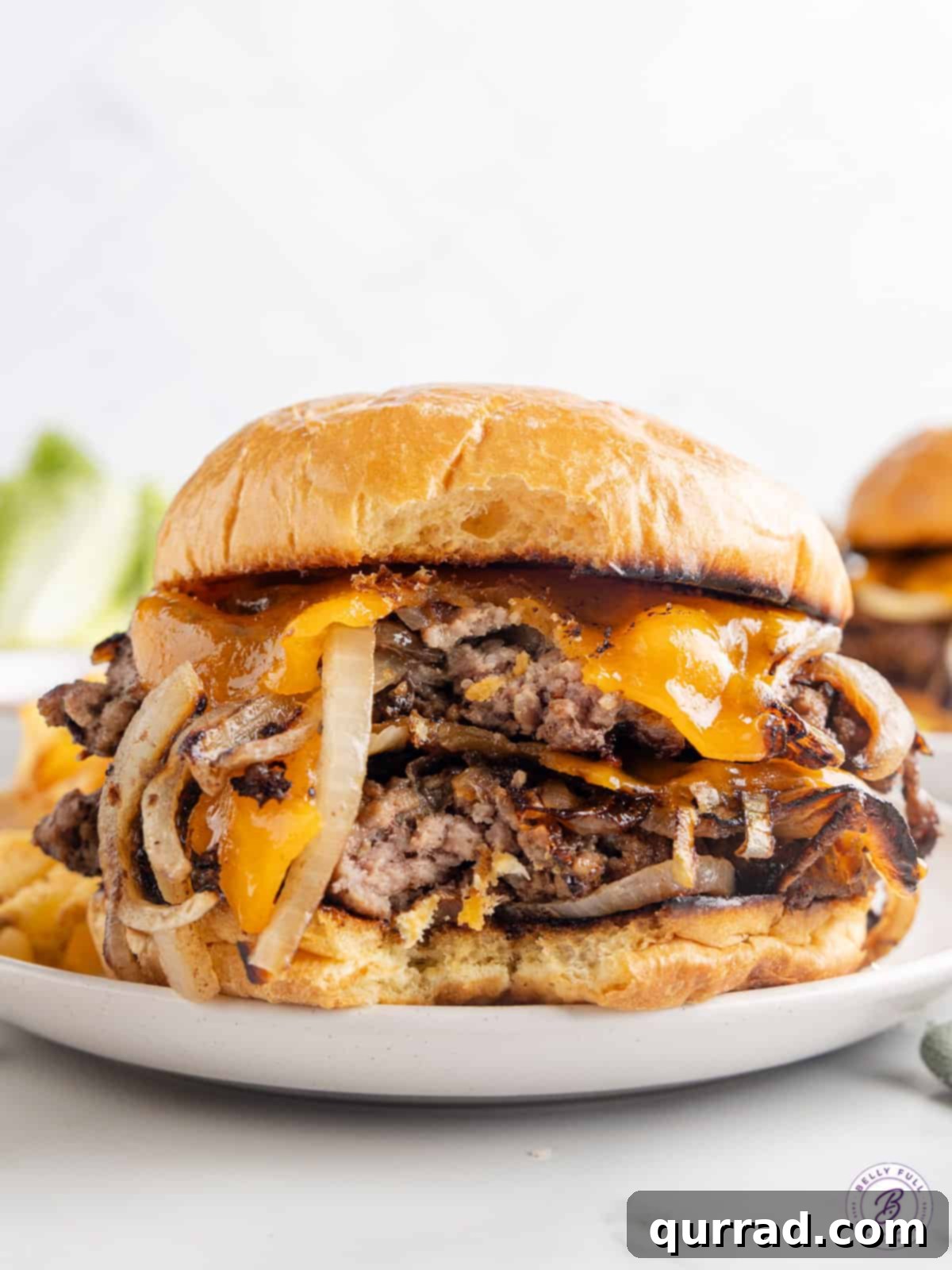 These Oklahoma Smash Burgers are burger patties smashed over thinly sliced onions, until the edges are crisp and the center remains juicy. A delicious double Oklahoma smash burger on a toasted bun with melted cheese, fresh lettuce, and tomato slices, ready to be enjoyed.