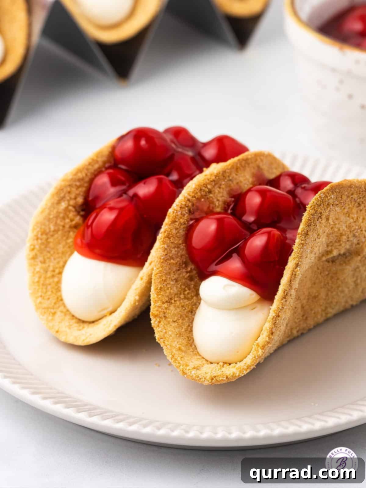 Sweet and tart Cherry Cheesecake Tacos, featuring crispy tortillas and creamy filling. Two cherry cheesecake tacos on a plate, showcasing their creamy filling and cherry topping.
