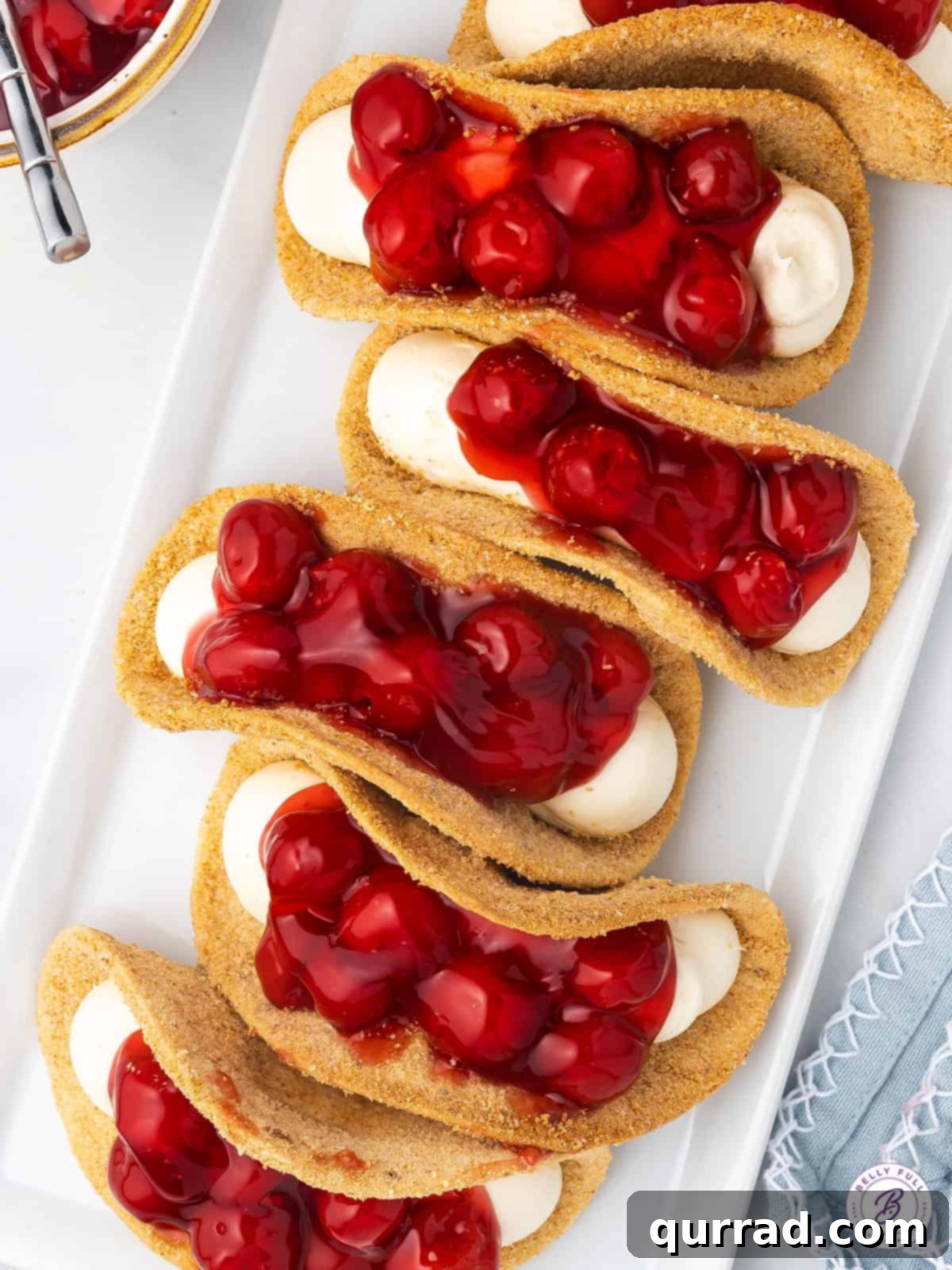 Six delicious Cherry Cheesecake Tacos, featuring sweet shells and creamy cherry filling. An overhead shot showing six perfectly arranged cherry cheesecake tacos on a white plate.