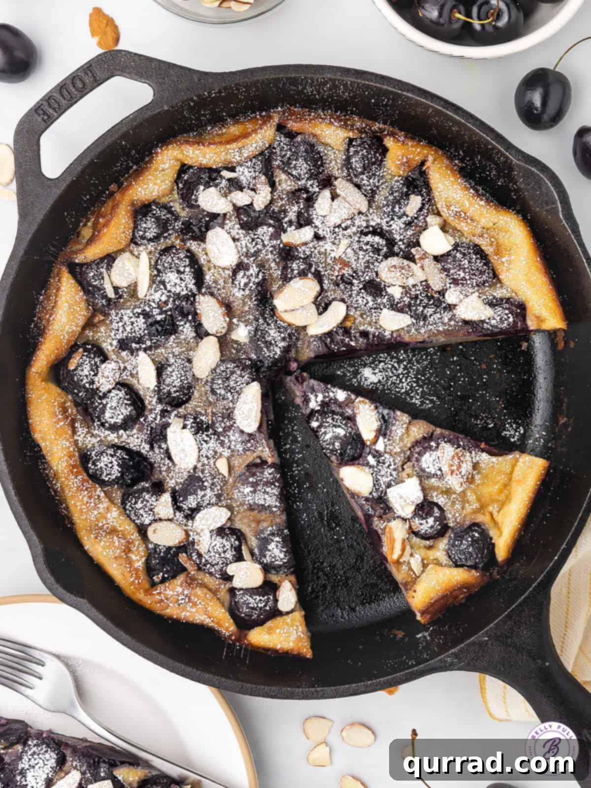 This Cherry Clafoutis recipe features a rich custard-like filling dotted with fresh tart cherries. Easy yet elegant! Cherry clafoutis in a cast iron skillet with two slices missing