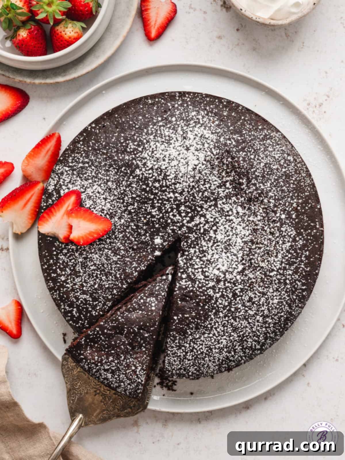 Experience an ultra-moist and intensely rich Vegan Chocolate Cake, made with premium cocoa powder, chopped vegan chocolate, and creamy almond milk. Overhead view of a beautifully presented vegan chocolate cake with one slice being served, showcasing its rich, dark color and moist texture.