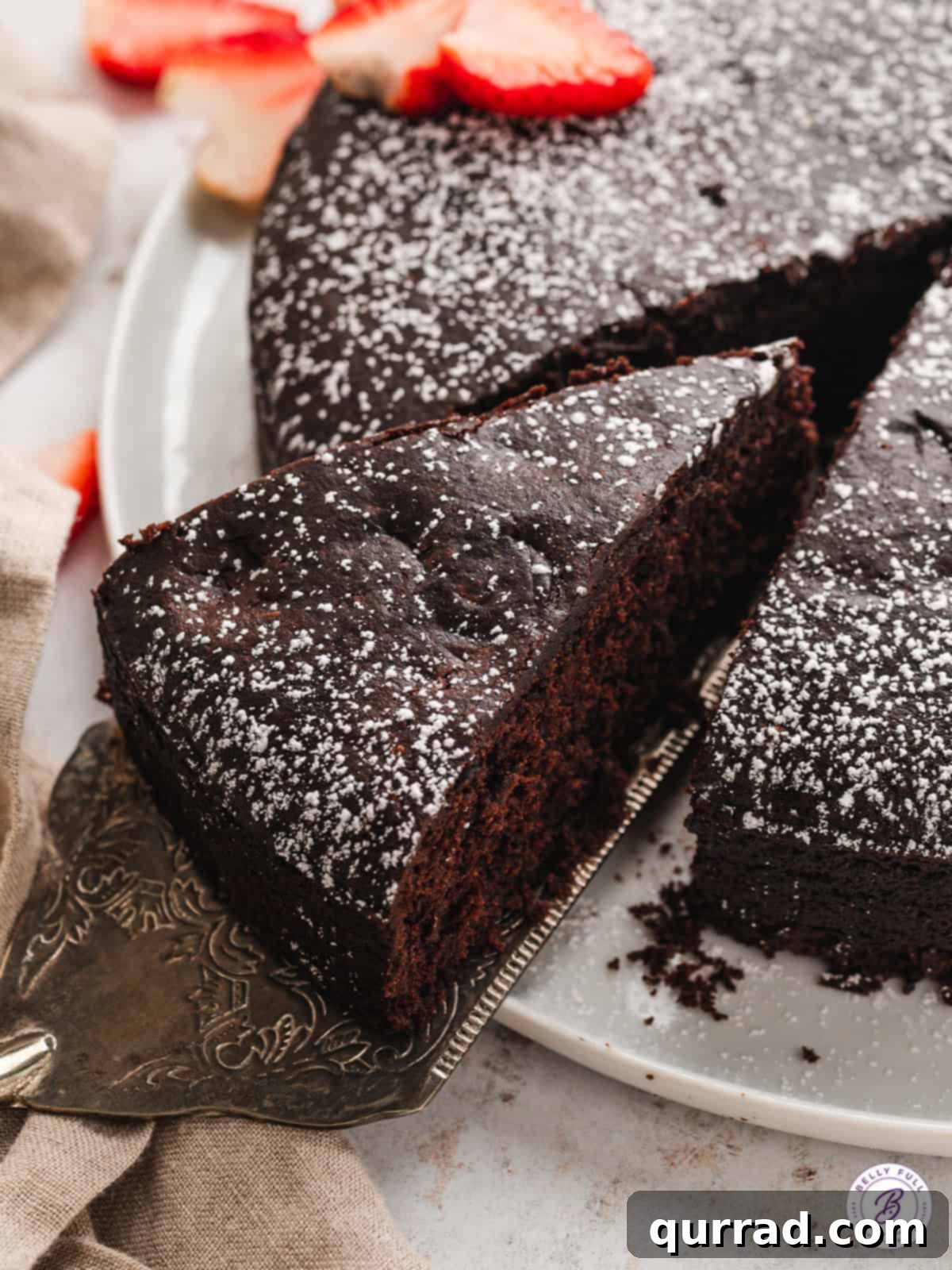 Indulge in this super moist, rich chocolate vegan cake, made with cocoa powder, chopped chocolate, and almond milk for an unforgettable flavor. A perfectly cut slice of eggless chocolate cake being delicately served from a whole cake, highlighting its uniform texture and tempting appearance.