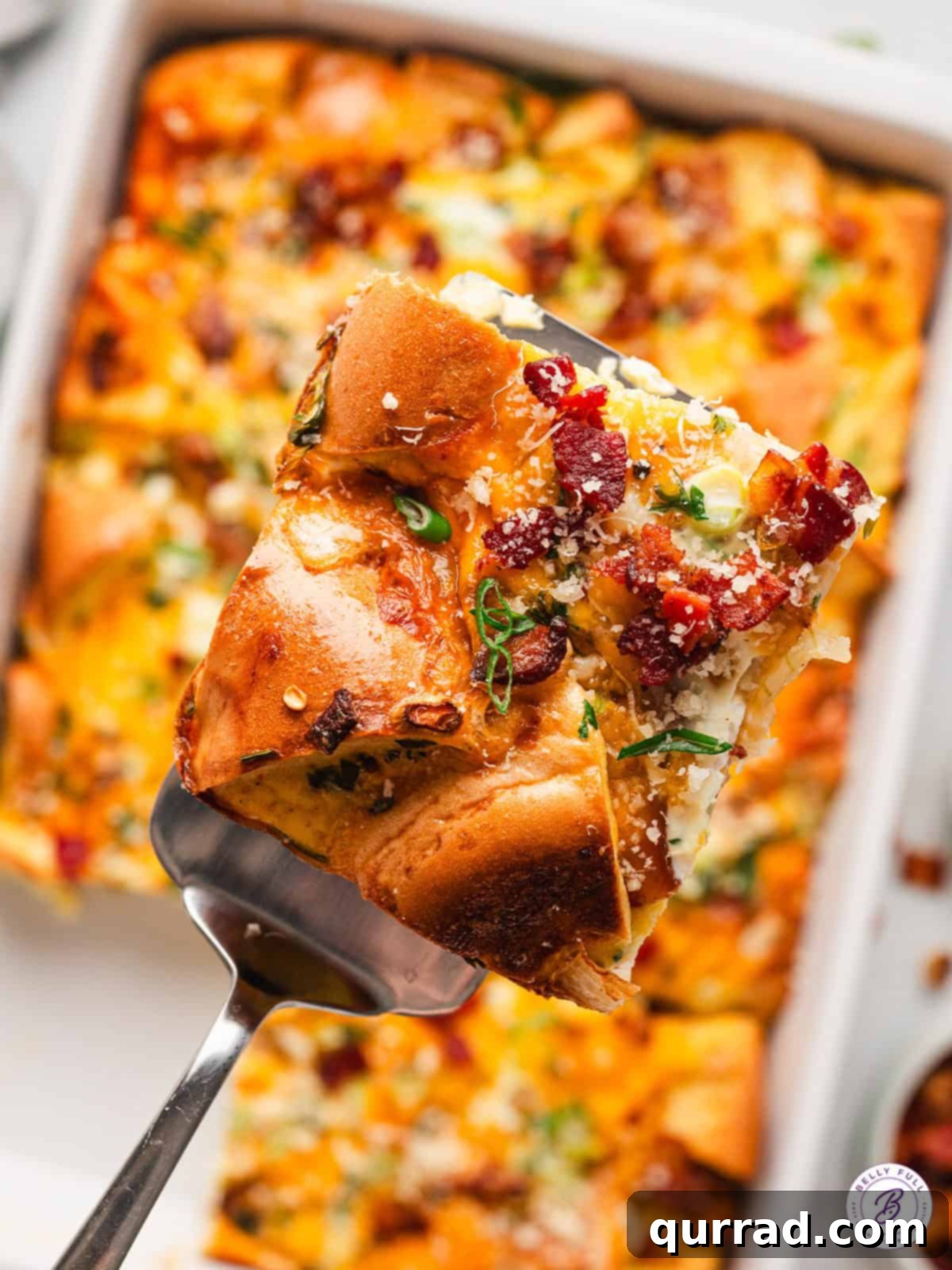 With thick-cut bacon, cheddar cheese, and a few spices, this Bagel Egg Bake is an easy savory option for breakfast or brunch. A perfectly portioned slice of bagel egg bake being served from a casserole dish