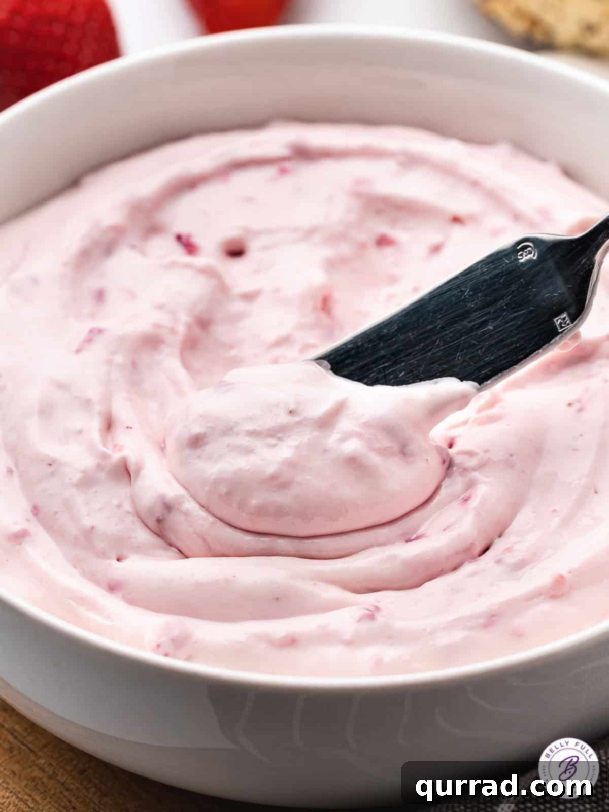 Made with fresh strawberries and powdered sugar, Strawberry Cream Cheese is light and fluffy with the perfect balance of sweet & tart flavors. A knife diving into a bowl of strawberry cream cheese, revealing its creamy texture and strawberry chunks.