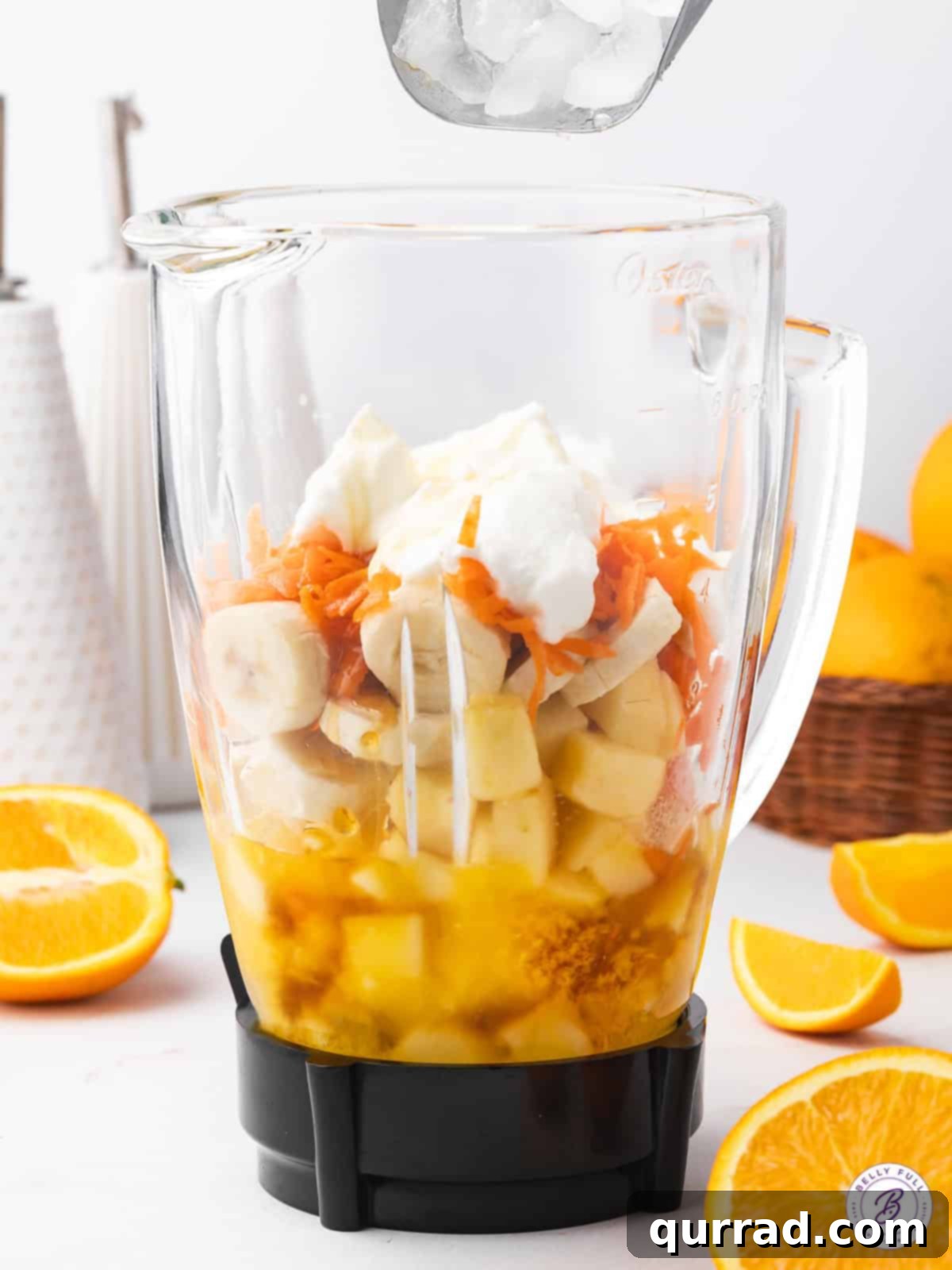 Liquid Sunshine 3 Assortment of fresh ingredients for an orange smoothie, including oranges, apple, carrot, banana, and yogurt, laid out on a surface.