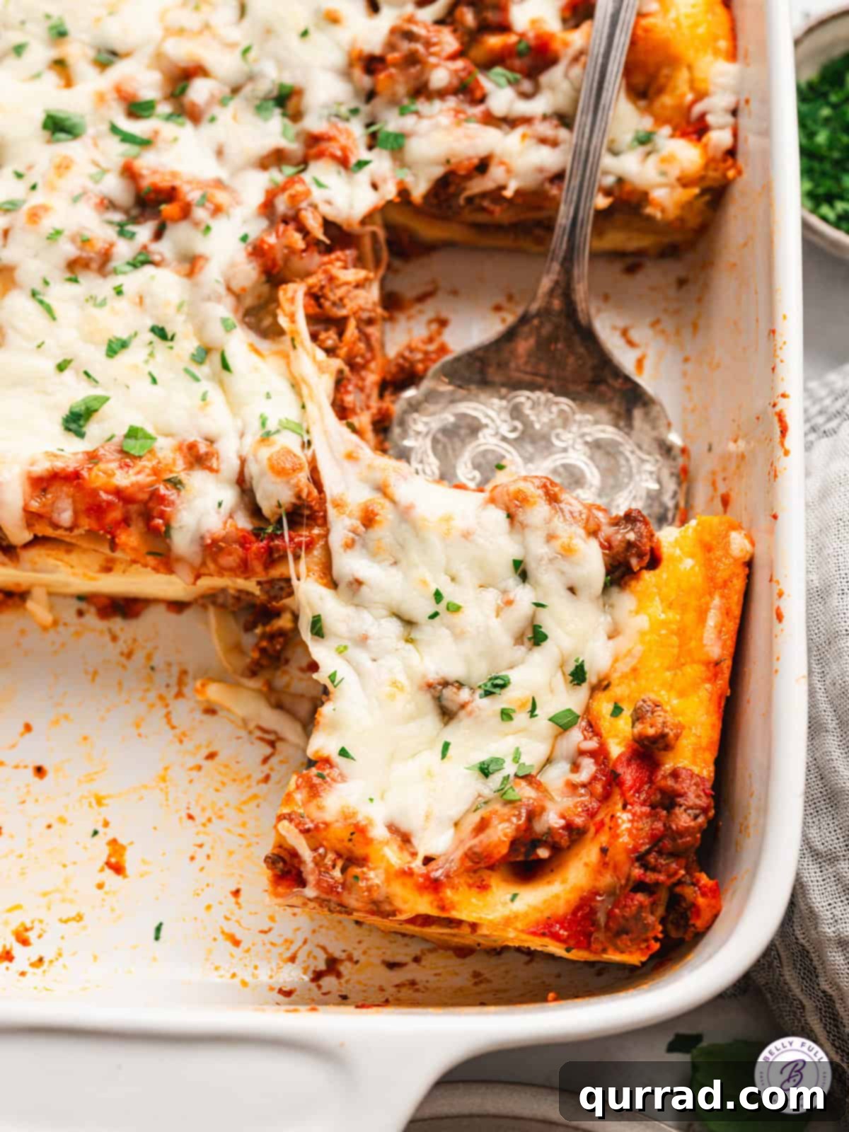 Lazy Day Lasagna is made with no-cook noodles, ricotta filling, and meat sauce. The easy lasagna recipe you didn't know you were missing! A hand serving a perfect slice of baked lazy day lasagna from a casserole dish