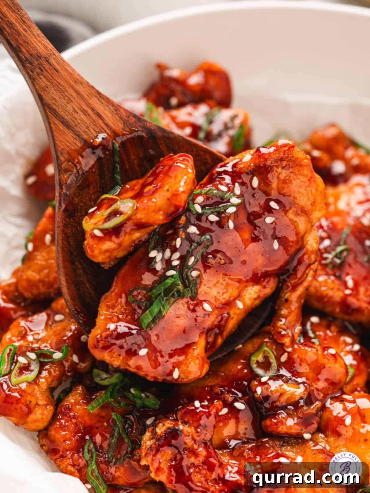 With honey, soy sauce, brown sugar, and sriracha, Sweet & Spicy Sticky Chicken offers the perfect balance of flavor & texture. A wooden spoon stirring sweet & spicy sticky chicken in a skillet, showcasing the rich, glossy sauce.