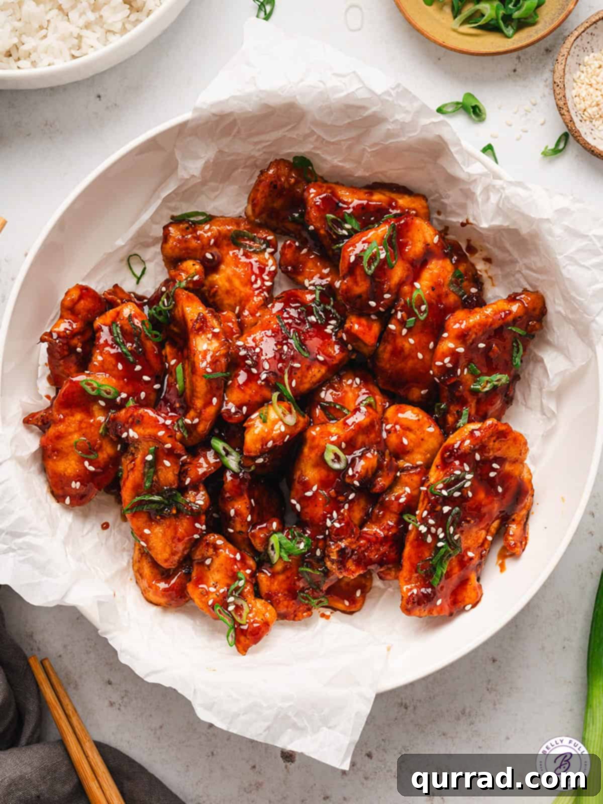 With honey, soy sauce, brown sugar, and sriracha, Sweet & Spicy Sticky Chicken offers the perfect balance of flavor & texture. A vibrant bowl of sweet and spicy sticky chicken, garnished with green onions and sesame seeds, ready to be served.