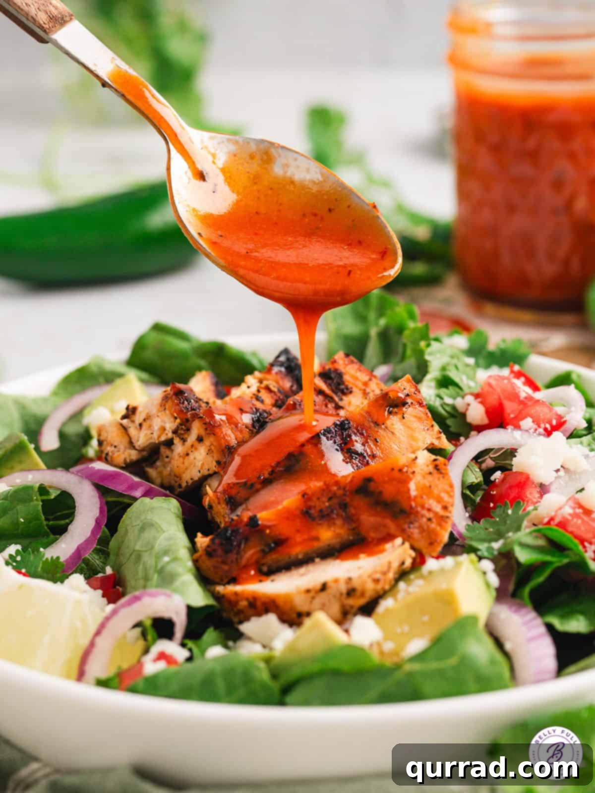 Chipotle honey vinaigrette is smokey and spicy with a tiny hint of sweetness. It's perfect for dressing salads, marinating meat, and more. Chipotle honey vinaigrette being drizzled generously over a colorful salad with grilled chicken, showing its rich texture and enticing appeal.