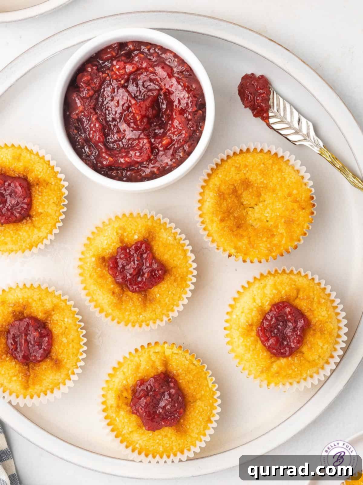 A cross between a creamy custard tart and an eggy macaroon, these Mini Coconut Cakes are a popular Portuguese dessert. A close-up shot of raspberry jam being delicately added to the top of golden mini coconut cakes.
