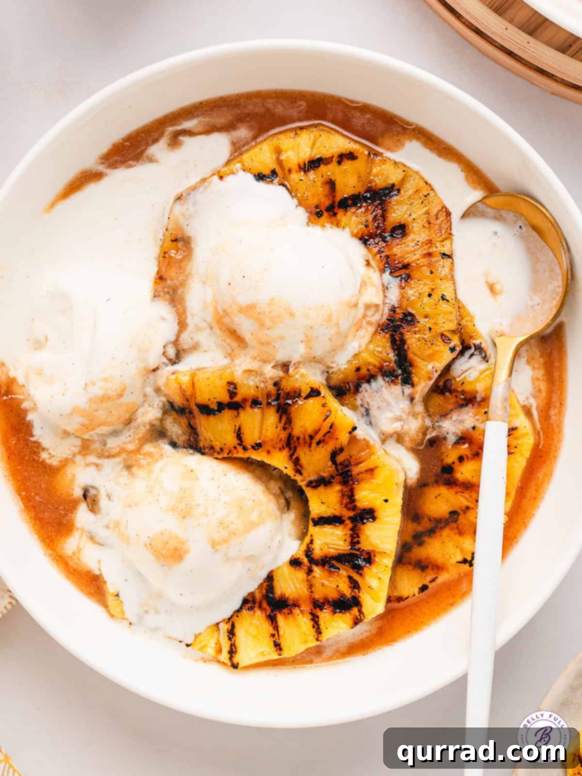Grilled pineapple, vanilla ice cream, and Pineapple Rum Sauce – a delightful dessert combination. A charming bowl of golden Pineapple Rum Sauce sits beside a plate of grilled pineapple and a scoop of vanilla ice cream, ready for serving.