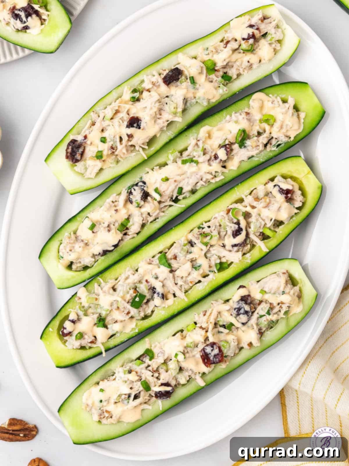 Cool, crunchy, and refreshing, these Chicken Salad Cucumber Boats are a fun and low-carb way to enjoy chicken salad. Easy lunch or snack! Overhead view of chicken salad cucumber boats on a serving platter, garnished with fresh herbs