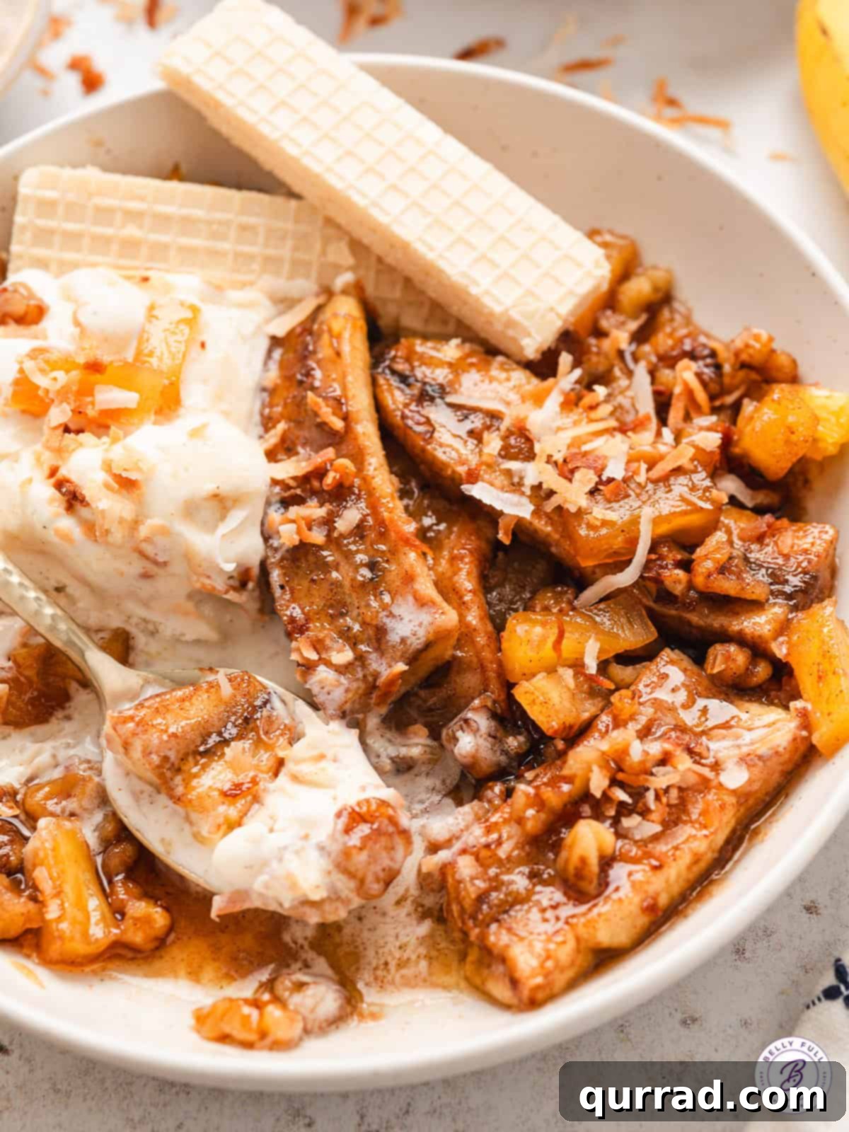 A close-up view of a bowl of warm pineapple bananas foster, topped with ice cream and toasted coconut.